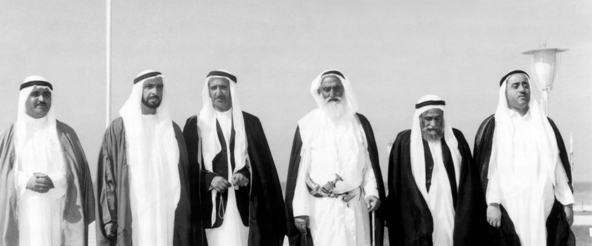  شيوخ الإمارات الست أمام علم دولة الإمارات العربية المتحدة في الثاني من ديسمبر 1971، بالأبيض والأسود.